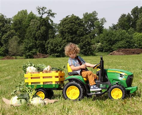 Bambino che guida un trattore elettrico Peg Perego con rimorchio